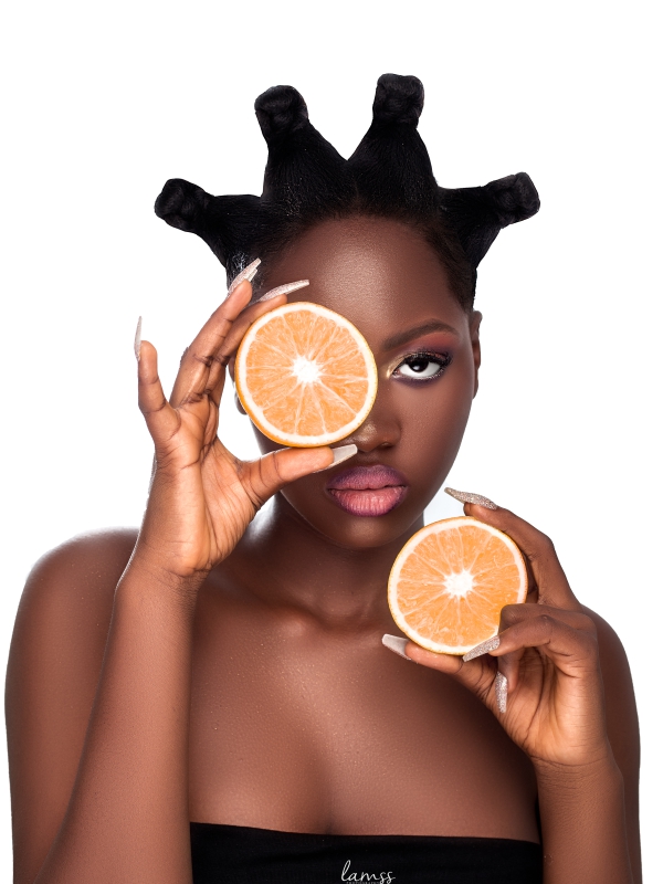 Close Up Of A Woman With An Intricate Braided Hairstyle Holding Sliced Grapefruit Halves Over Her Eyes.